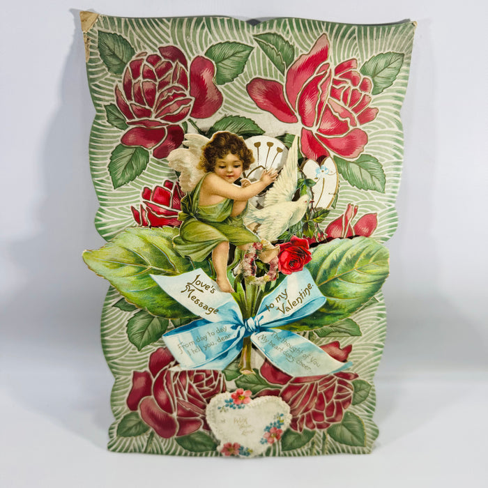 Antique Victorian stand-up Valentine card with pop-out cherub and white dove, red roses, green leaves, and blue ribbon reading “Love’s Message” and “to my Valentine.”