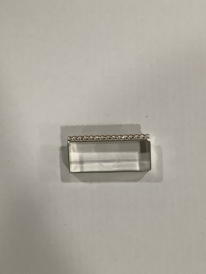 A small rectangular clear acrylic or glass block with a silver metal frame and a decorative beaded top edge, photographed on a plain light gray background.